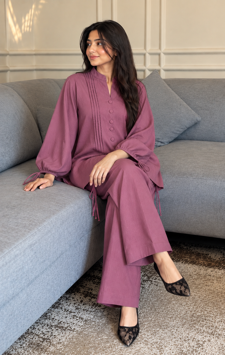 Dusty rose crushed linen co-ord set by Numaish, styled with black lace pointed heels, seated on a grey sofa